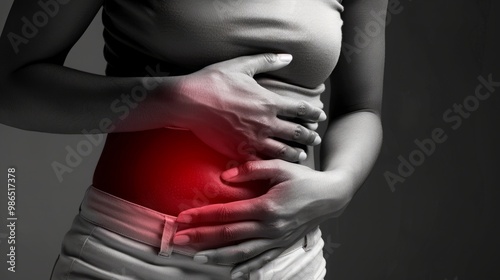 A woman's hand is clutching her abdomen in pain. The red highlight on her stomach indicates where the pain is. This is a common symptom of appendicitis, IBS, or other stomach illnesses.