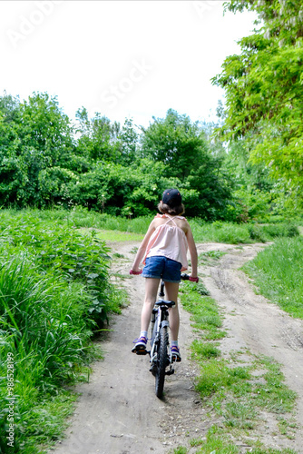 Young girl cyclist enjoy the beautiful sunrise on summer forest trail. Close-up portrait of a happy little girl in a helmet on a bicycle. High quality photo