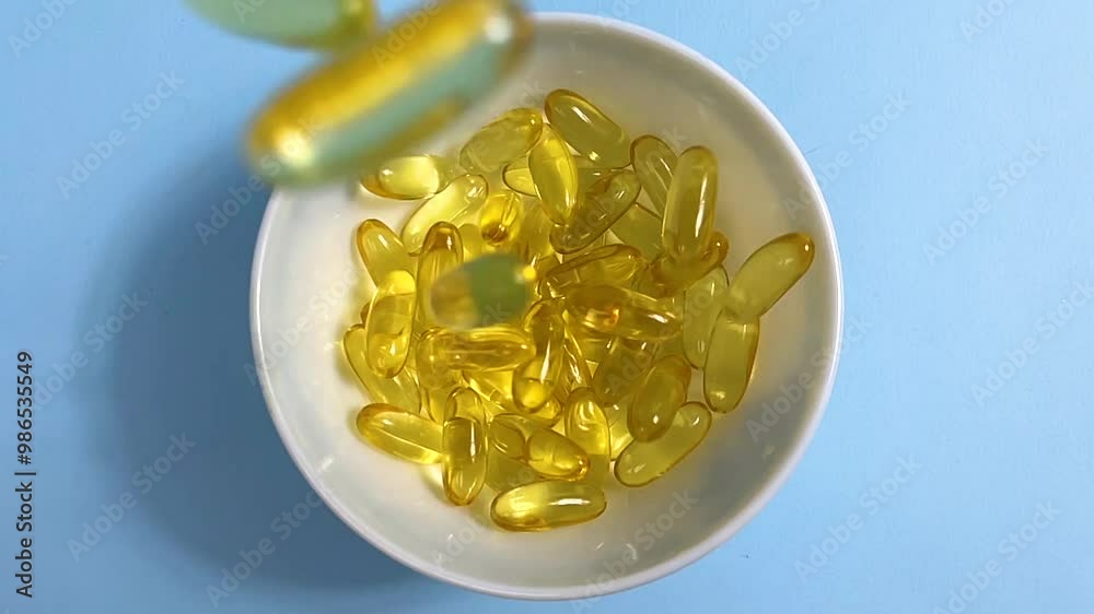 Yellow transparent capsules with liquid Omega 3 fall into a white bowl. Slow motion. Close up. Concept of maintaining and improving health. Fish oil is an essential supplement for wellness. Yellow transparent capsules with liquid Omega 3 fall into a white bowl. Slow motion. Close up. Concept of maintaining and improving health. Fish oil is an essential supplement for wellness.