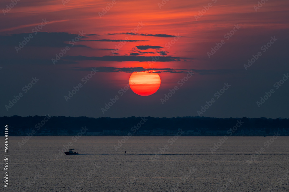 The sun is enormous and pink during a sunset over the water of the Assawoman bay in Ocean City, Maryland.