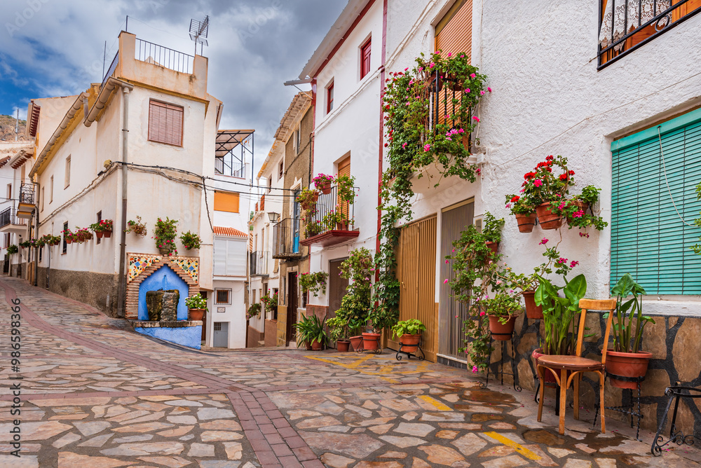 Street with a fountain and decorated with flower pots hanging from the walls of the houses in the town of Castril, Granada. Street with a fountain and decorated with flower pots hanging from the walls of the houses in the town of Castril, Granada.
