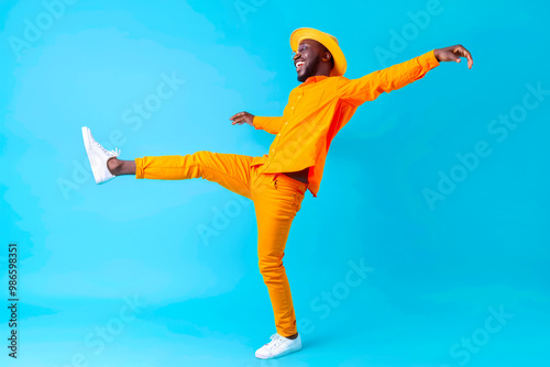 Full body side view smiling fun cheerful young happy african american man in orange shirt hat stand on toes leaning back dancing fooling around isolated on plain pastel light blue background studio. photo