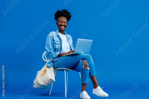 Full body young smiling student fun happy black woman in casual clothes shirt white t-shirt sit in bag chair hold use work on laptop pc computer isolated on plain dark blue background studio portrait.