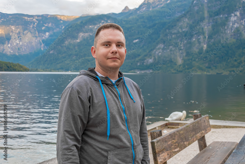 Fototapeta premium A 25-30 year old man stands at a wooden pier near a quiet mountain lake,