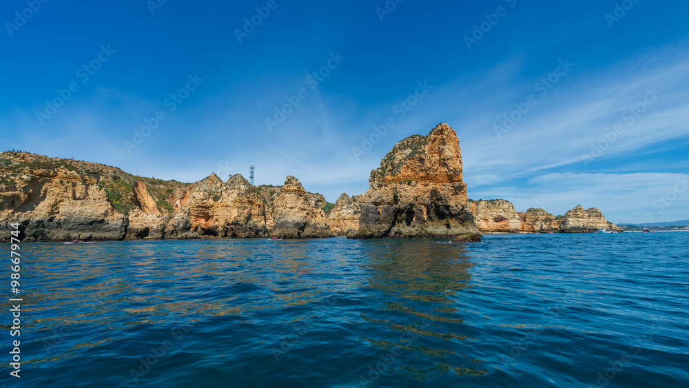 Scenic view of the Algarve coastline's rock formations at sunrise, with calm blue waters and a clear sky, Portugal. Scenic view of the Algarve coastline's rock formations at sunrise, with calm blue waters and a clear sky, Portugal.