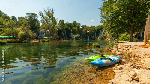 Εκτύπωση καμβά Kayaks by tranquil riverbank with scenic waterfall backdrop, perfect for summer adventure