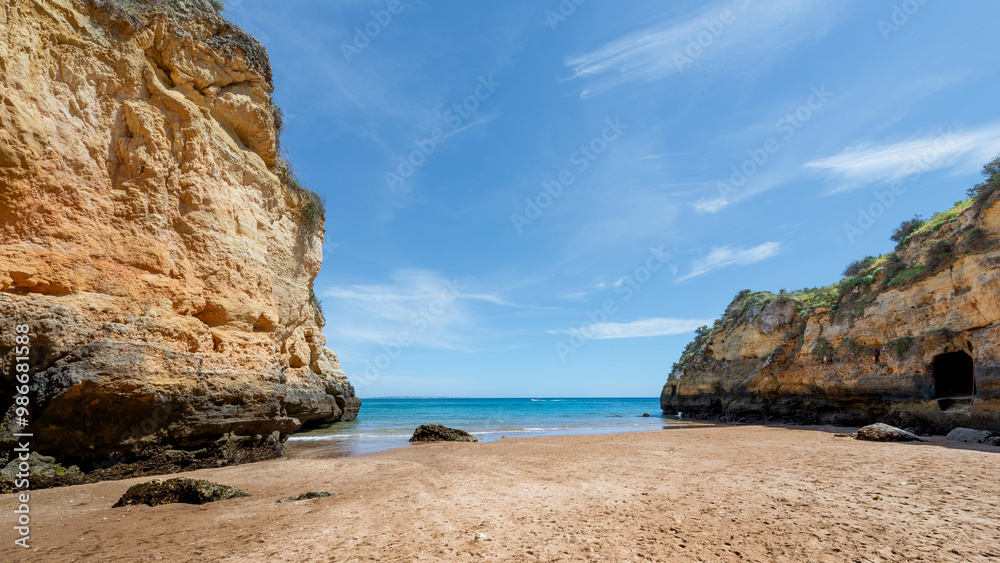 Scenic Algarve beach with golden sand, turquoise water and towering cliffs under blue sky. Scenic Algarve beach with golden sand, turquoise water and towering cliffs under blue sky.