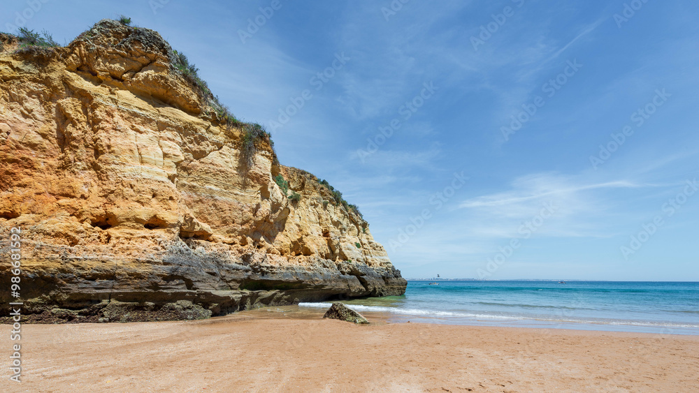 Scenic Algarve beach with golden sand, turquoise water and towering cliffs under blue sky. Scenic Algarve beach with golden sand, turquoise water and towering cliffs under blue sky.