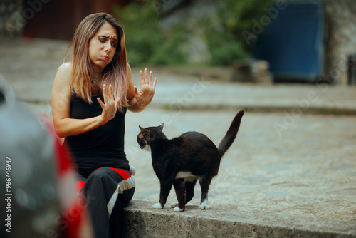 Stressed Woman Disliking a Cat That Follows Her Around. Unhappy lady saying no to a kitten waiting to be friends 
 photo