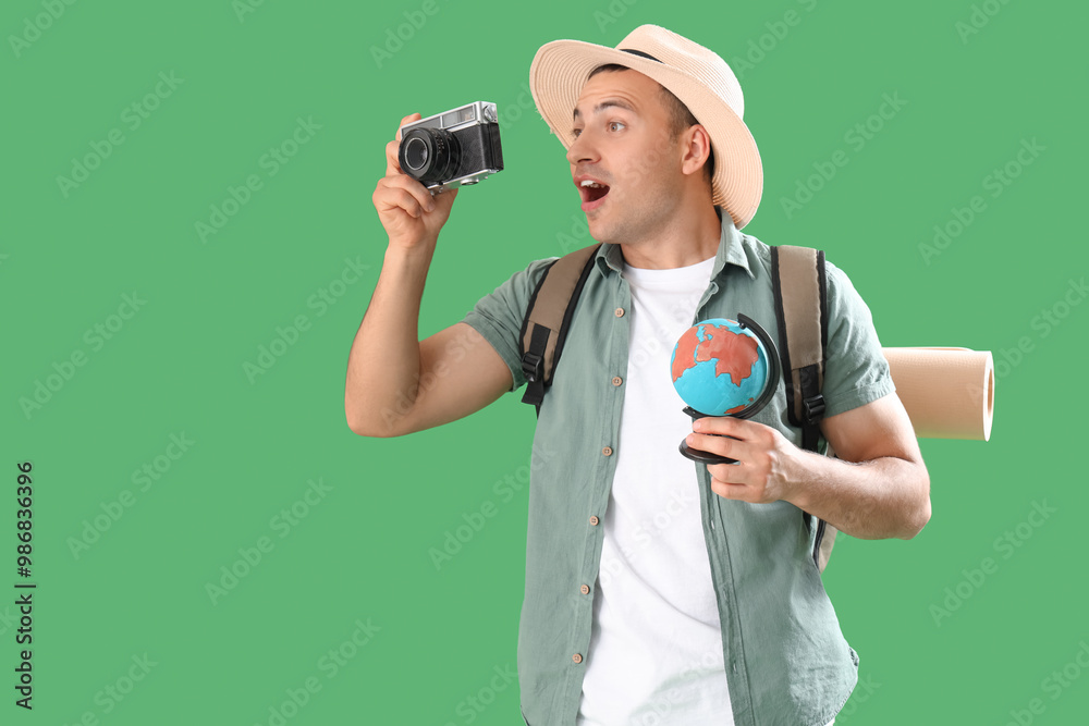 Surprised male tourist with globe and photo camera on green background Surprised male tourist with globe and photo camera on green background