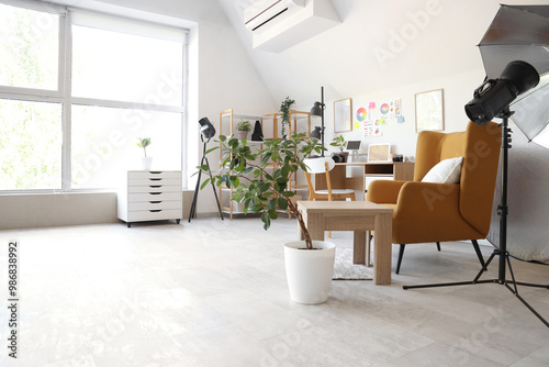 Photographer workplace with armchair, laptop and lighting equipment in modern photo studio