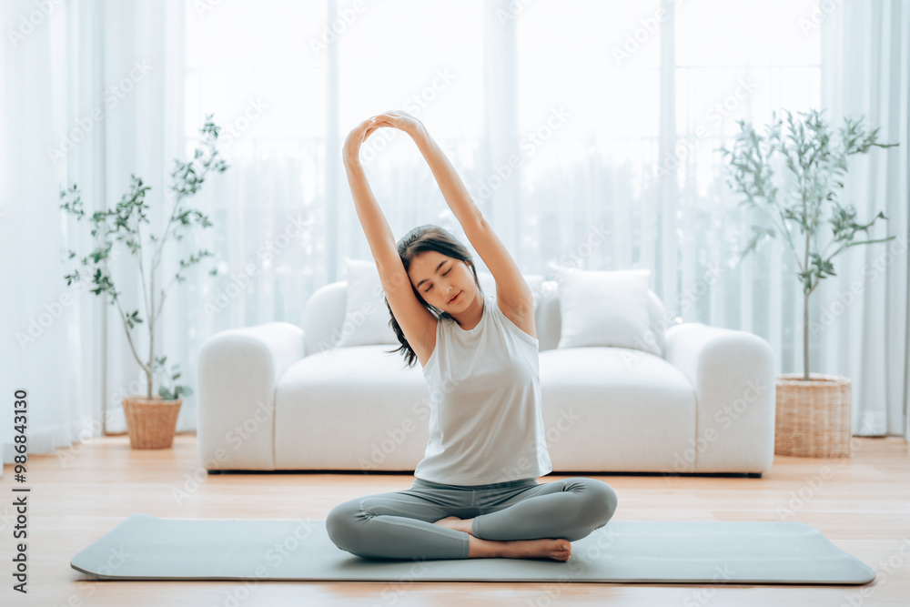 Happy young Asian woman practicing yoga and shoulder stretching at home sitting on floor in living room Happy young Asian woman practicing yoga and shoulder stretching at home sitting on floor in living room