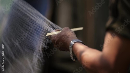 Close-up view of a man weaving a traditional fishing net by hand, using techniques from an Asian village in a Nepali rural setting photo