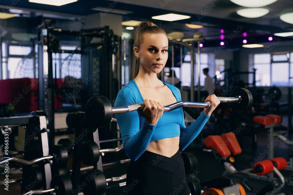 Fototapeta premium A young woman lifts weights in a modern gym during a fitness session