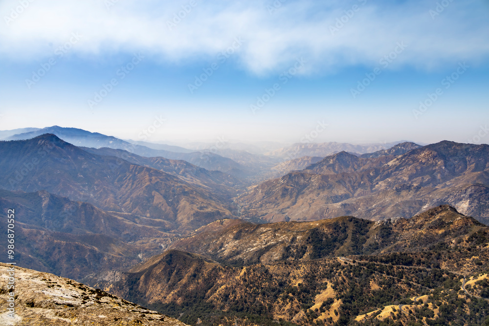 Fototapeta premium View of the Sierra Nevada mountain range from Moro Rock Trail in Sequoia National Park, California, showcasing forested slopes and distant peaks under a clear blue sky.