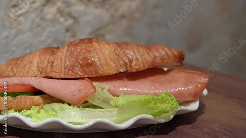 Close-up view of a croissant with chicken ham ,tomato slice, and salad coral.