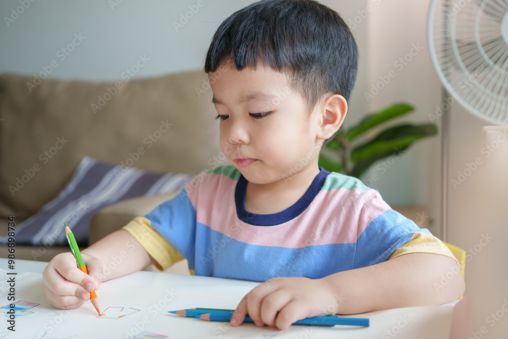 Asian boy is sitting at a table and coloring with colored pencil on paper. Concept of creativity and playfulness Asian boy is sitting at a table and coloring with colored pencil on paper. Concept of creativity and playfulness