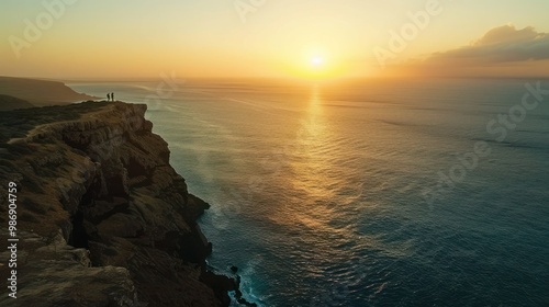 A dramatic cliffside overlooking the ocean, with a couple enjoying the view and the sun setting in the distance, casting a beautiful glow.