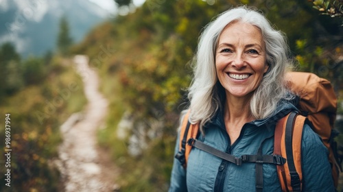 Smiling grey-haired woman hiking on a scenic trail, appreciating the beauty of the outdoors.