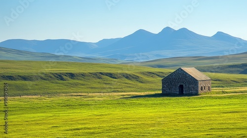 A captivating photograph of a remote, untouched highland plateau with rolling green hills and a solitary, ancient stone structure. The expansive, clear blue sky and the distant mountain peaks add to photo