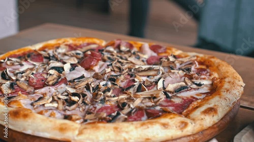 Close-up shot of a pizza with mushrooms, salami, and bacon on a wooden board. This footage is perfect for food blogs, commercials, and social media posts.
