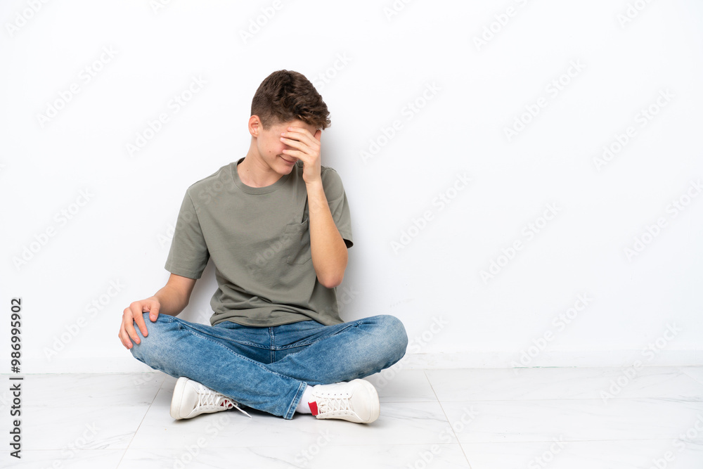 Teenager Russian man sitting on the floor isolated on white background laughing Teenager Russian man sitting on the floor isolated on white background laughing