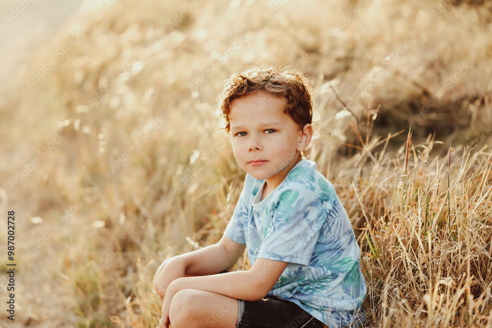 Little aboriginal Australian boy sitting in long dry grass golden afternoon light Little aboriginal Australian boy sitting in long dry grass golden afternoon light