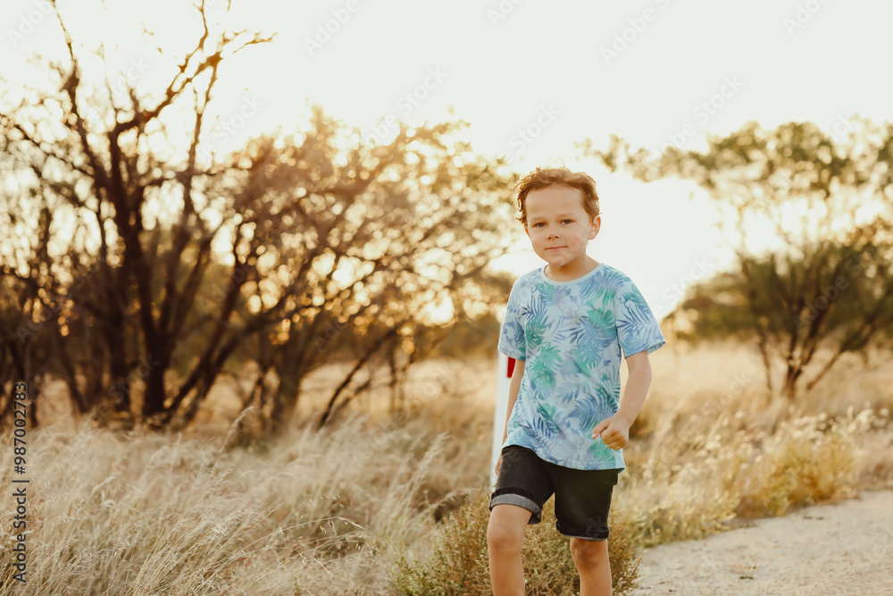 Little boy walking along rural gravel road in golden afternoon light Little boy walking along rural gravel road in golden afternoon light