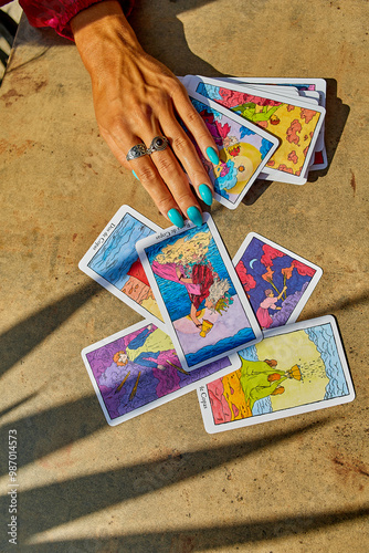 PALMA, SPAIN-August 29,2024;A hand with turquoise nails and a silver ring rests on scattered tarot cards, symbolizing divination, intuition, and the spiritual practice of tarot reading