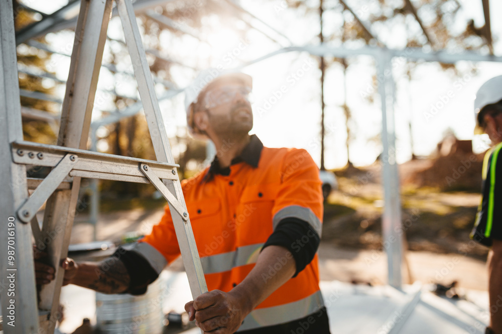 Construction worker holding a steel ladder while looking up. Construction worker holding a steel ladder while looking up.