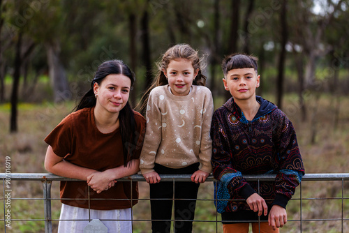Three aboriginal kids leaning on fence together in paddock in winter