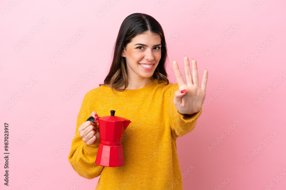 Young Italian woman holding a coffee maker isolated on pink background happy and counting four with fingers Young Italian woman holding a coffee maker isolated on pink background happy and counting four with fingers
