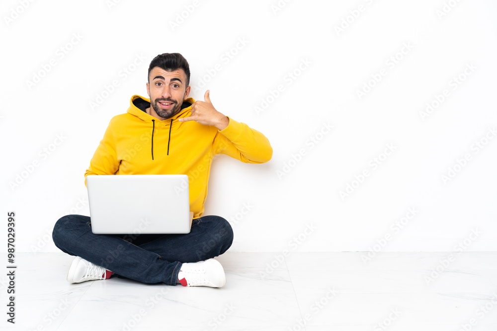 Caucasian man sitting on the floor with his laptop making phone gesture. Call me back sign Caucasian man sitting on the floor with his laptop making phone gesture. Call me back sign