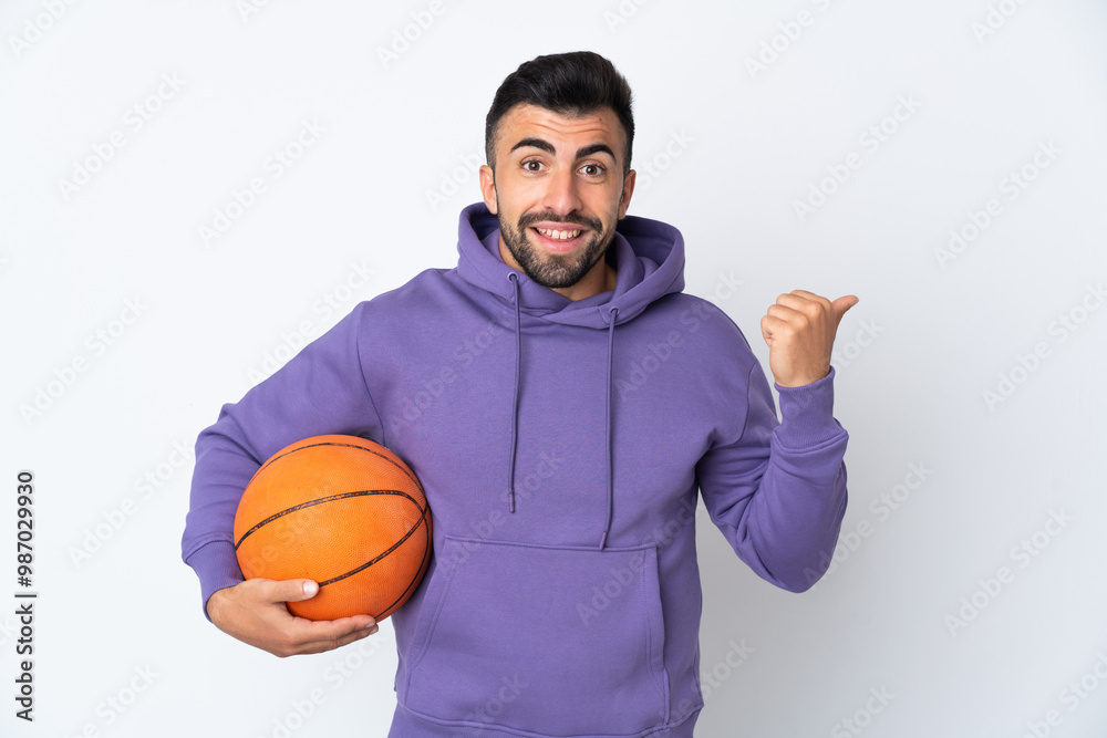 Man playing basketball over isolated white wall pointing to the side to present a product Man playing basketball over isolated white wall pointing to the side to present a product