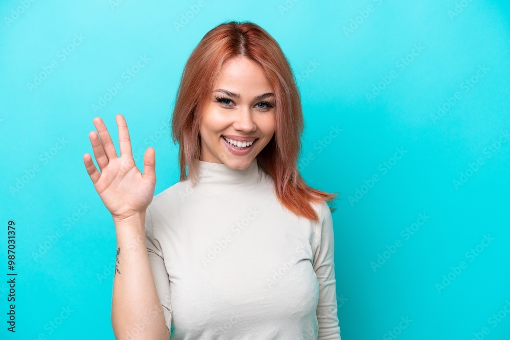 Fototapeta premium Young Russian woman isolated on blue background saluting with hand with happy expression