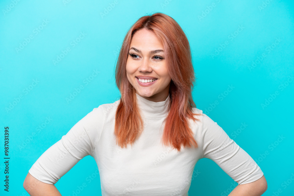 Young Russian woman isolated on blue background posing with arms at hip and smiling Young Russian woman isolated on blue background posing with arms at hip and smiling