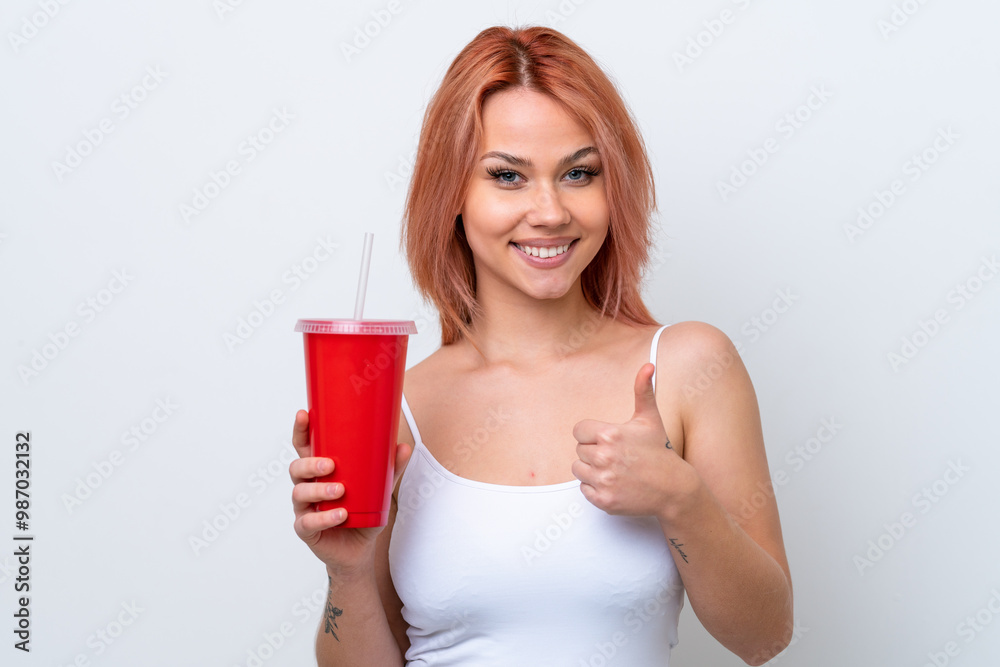 Young Russian woman holding soft drink isolated on white background with thumbs up because something good has happened Young Russian woman holding soft drink isolated on white background with thumbs up because something good has happened