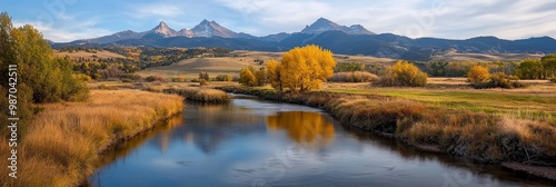  A river runs through two lush, green fields Trees border the scene, and mountains rise in the background
