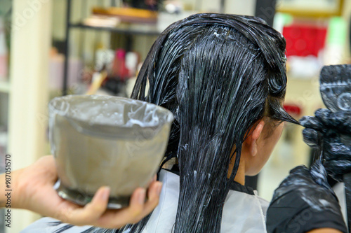 Two hairdressers are applying keratin hair straightening solution to the hair of a female customer in a hair care beauty salon in Thailand. photo