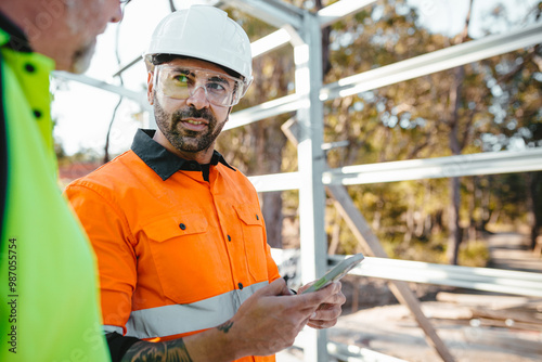 Two men wearing safety gears on the site with one holding a mobile device.