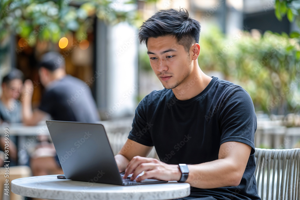An oriental man is sitting at a table with a laptop, looking at the screen. An oriental man is sitting at a table with a laptop, looking at the screen.