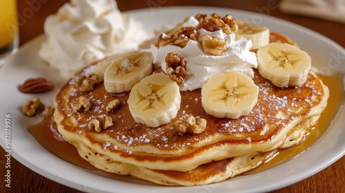 A plate of fluffy pancakes topped with sliced bananas, walnuts, and a drizzle of maple syrup, served with a side of whipped cream