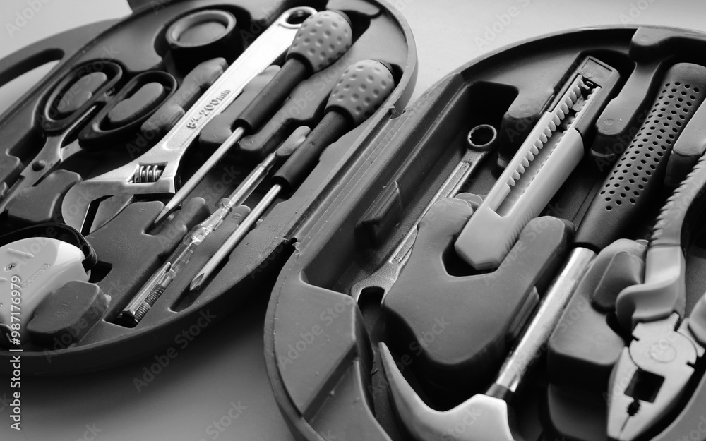 Fototapeta premium Hammer, pliers, mounting knife, scissors, electrical tape, voltage tester, measure roller and screwdrivers in a toolbox grayscale stock photo