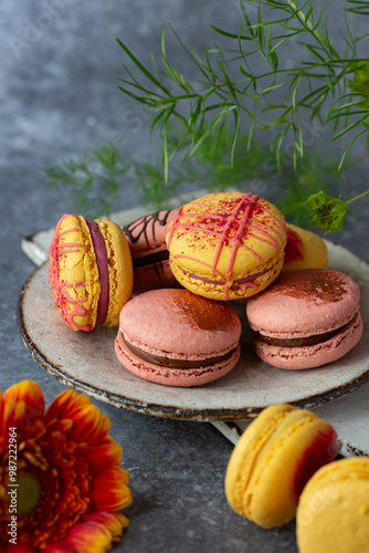 French macaroons of yellow colour on light grey ceramic booard with orange red flowers on blue grey  background  photo