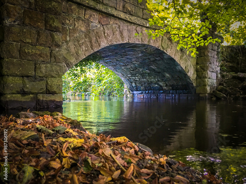 Stone arch bridge over a calm river in Leitrim, surrounded by trees and autumn leaves.