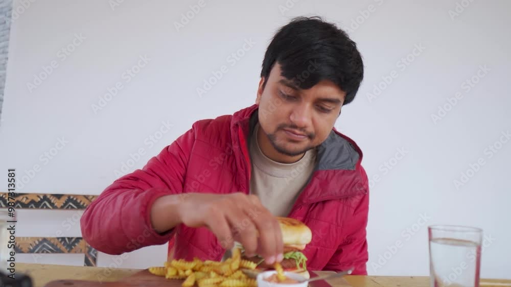 Indian man eating French fries and burger while sitting at a café in Manali, Himachal Pradesh, India. Indian man eating fast food in a restaurant. Man enjoys junk food while sitting outside. Indian man eating French fries and burger while sitting at a café in Manali, Himachal Pradesh, India. Indian man eating fast food in a restaurant. Man enjoys junk food while sitting outside.