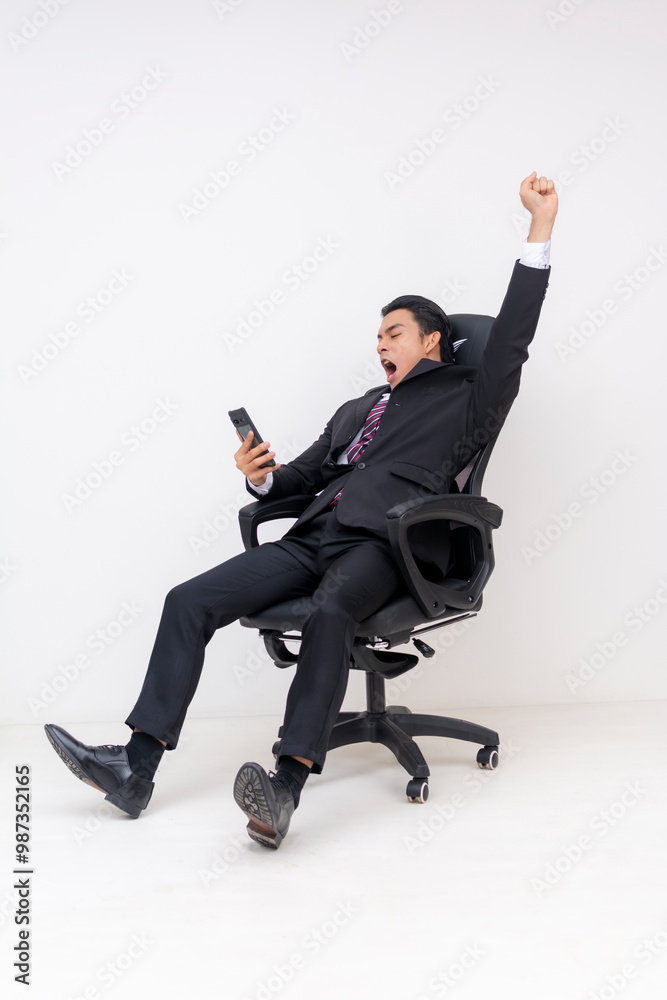 Tired young businessman yawning while seated on office chair holding cellphone Tired young businessman yawning while seated on office chair holding cellphone