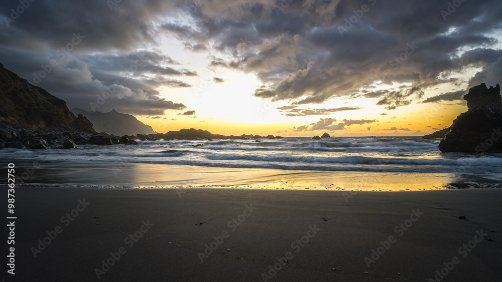 Obraz premium Tenerife, June 2022: A rock strewn bay at sunset with the tide rolling in