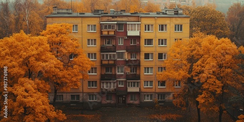 A picturesque autumn scene featuring a multi-story apartment building surrounded by vibrant orange foliage, highlighting the seasonal transition