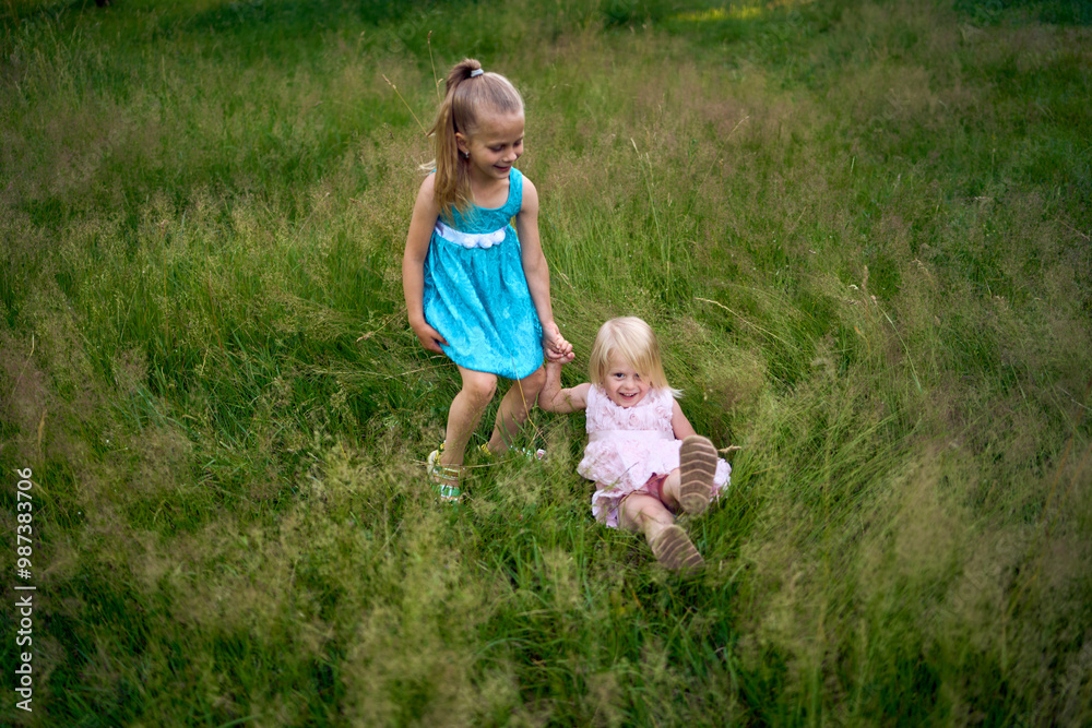 Fototapeta premium little sisters in dresses playing together in the tall grass